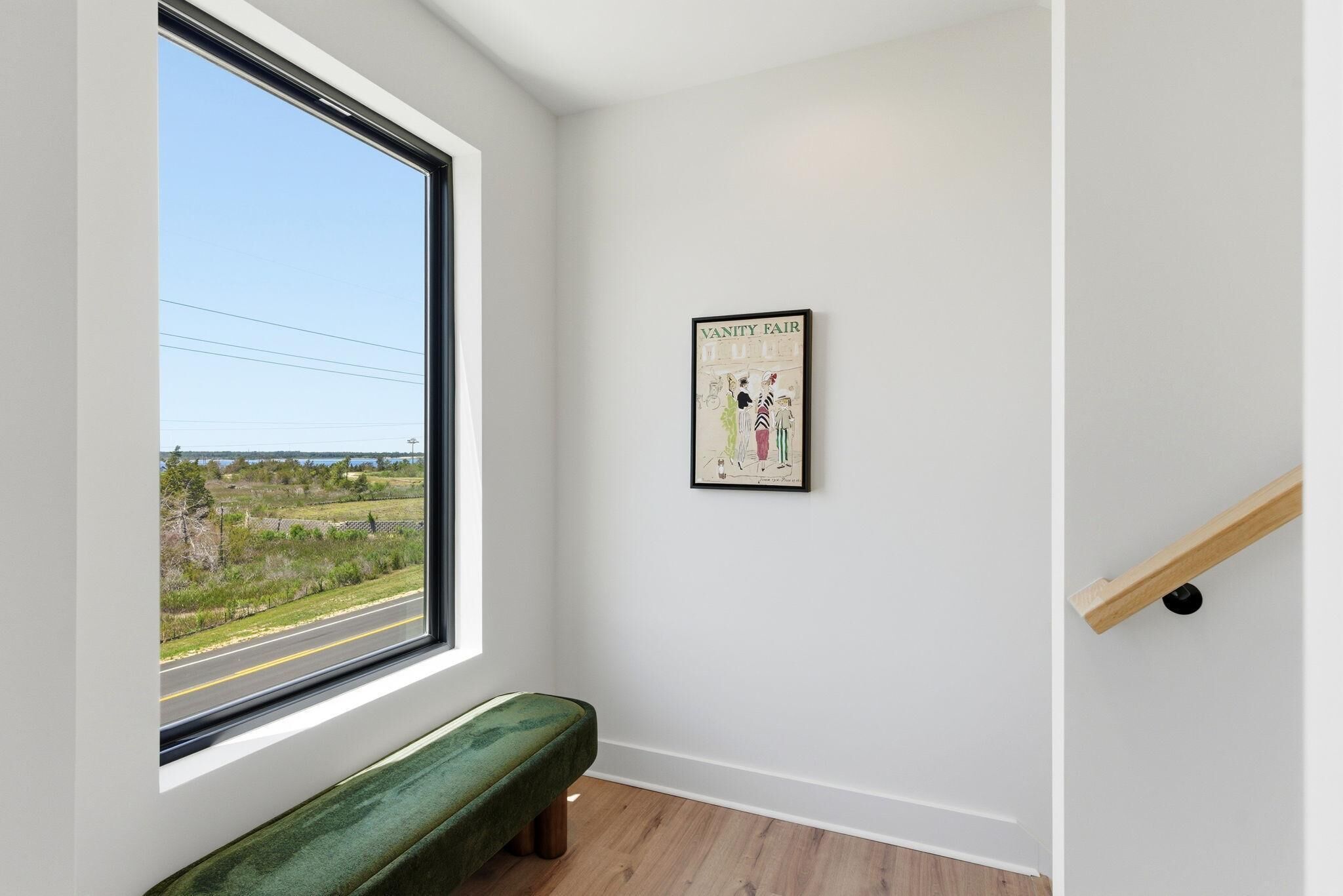 A room with a large window, a bench, a framed artwork, and a wooden handrail.