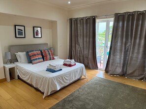 Ein Schlafzimmer mit einem Bett, Kissen, einem Nachttisch, einer Lampe und Blick durch ein Fenster mit Vorhängen.