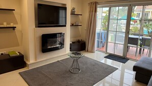 Ein modernes Wohnzimmer mit Flachbildfernseher, Kamin und einer Schiebetür zu einem Außenbereich.