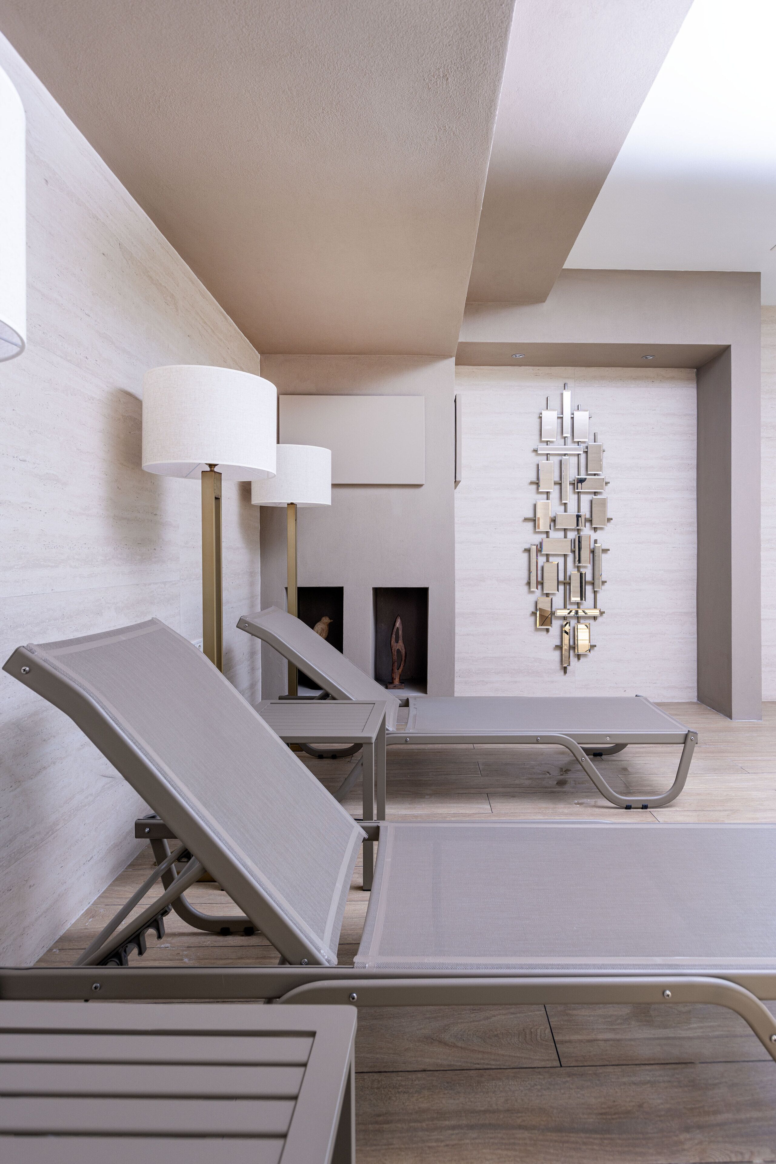 Une chambre moderne au design minimaliste, comprenant un coin salon avec des fauteuils inclinables, un luminaire décoratif fixé au mur et une cheminée.