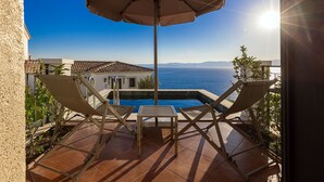 A terrace with a pool, two lounge chairs, an umbrella, and a view of the sea. - Hotel Jirasol (Çeşme)