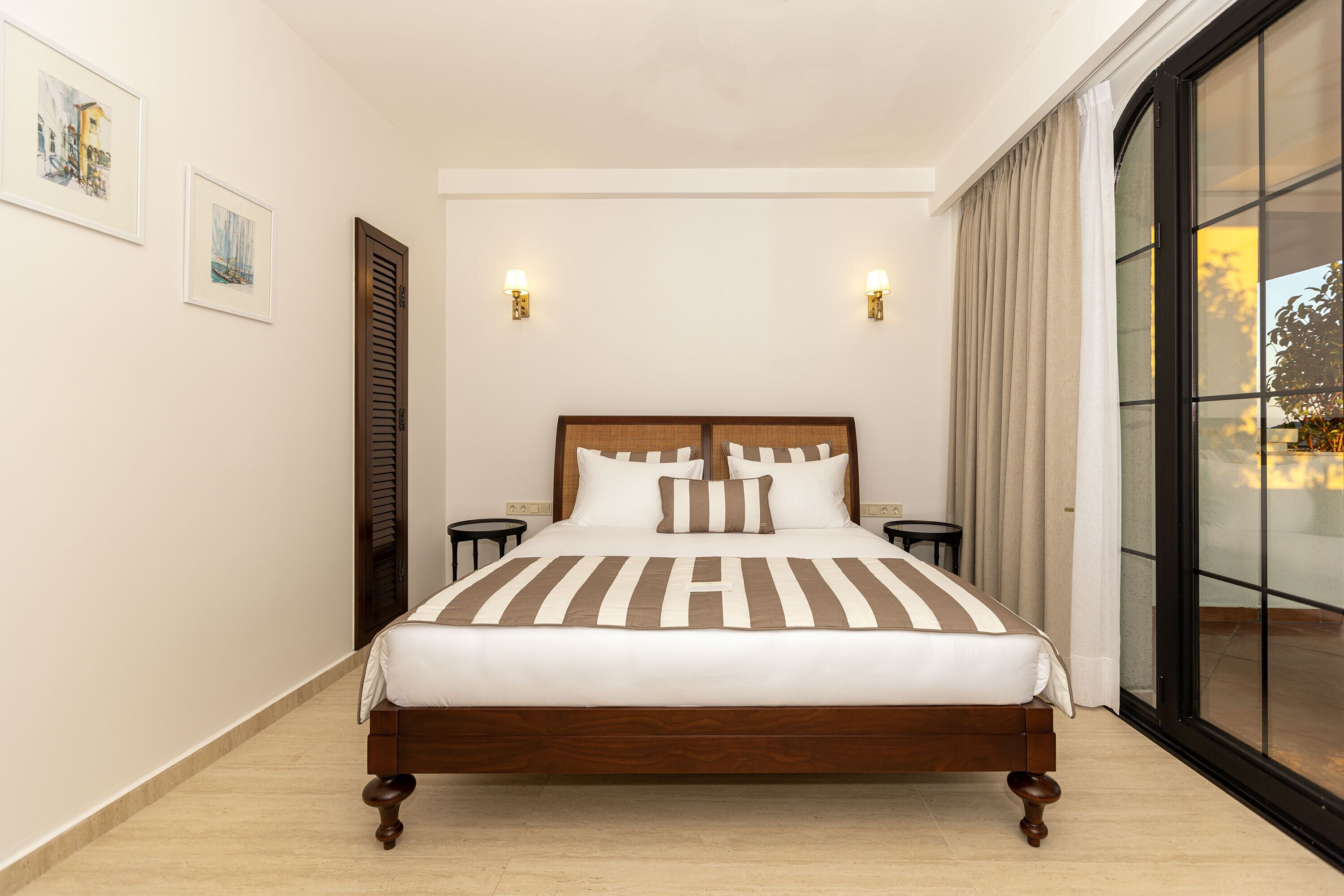 A hotel room with a large bed, two bedside tables, a window with curtains, and wall-mounted lights.
