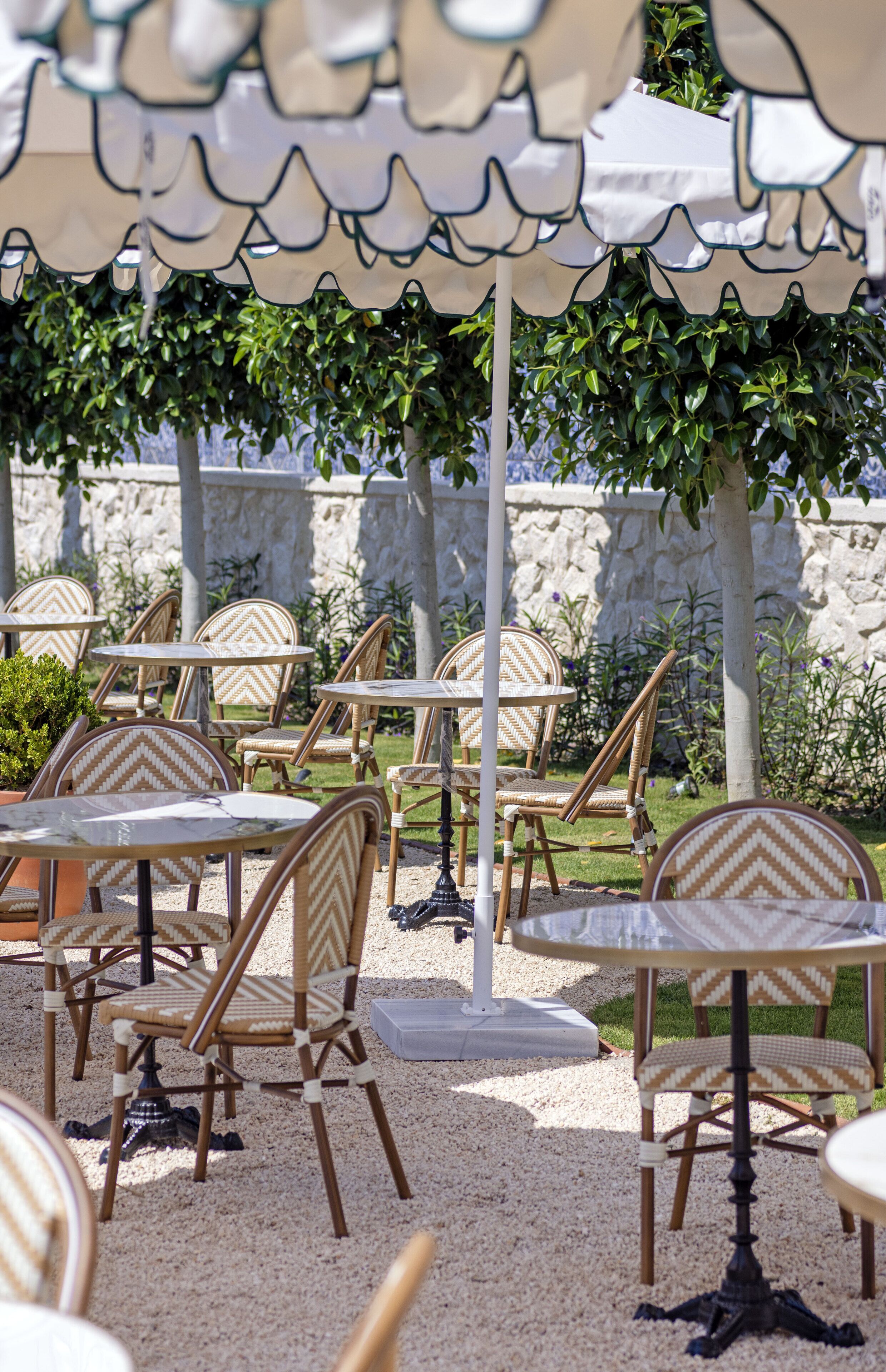 Espace extérieur aménagé avec des chaises et des tables en osier, des parasols et un mur de pierre en arrière-plan.