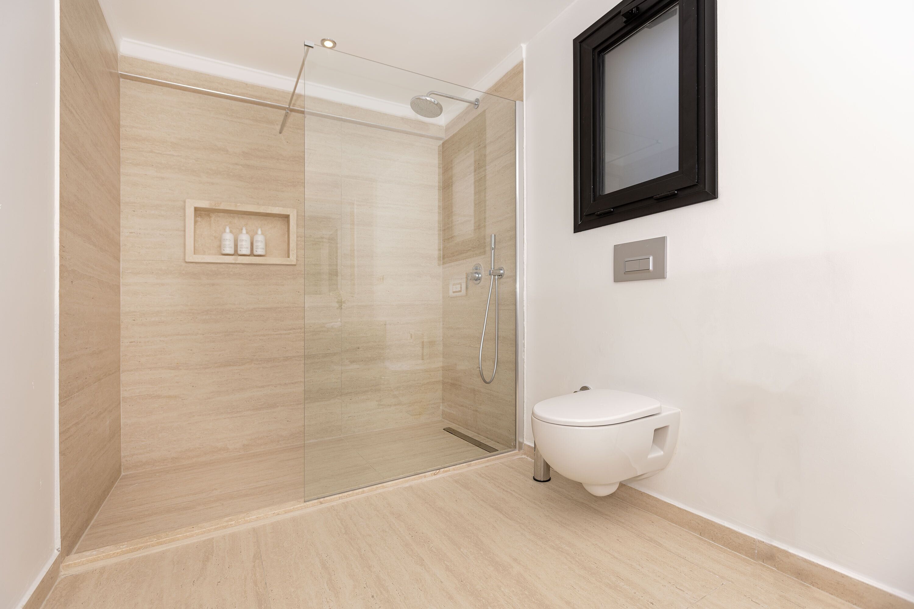 Un baño moderno con ducha de vidrio, inodoro blanco y espejo con marco en la pared.