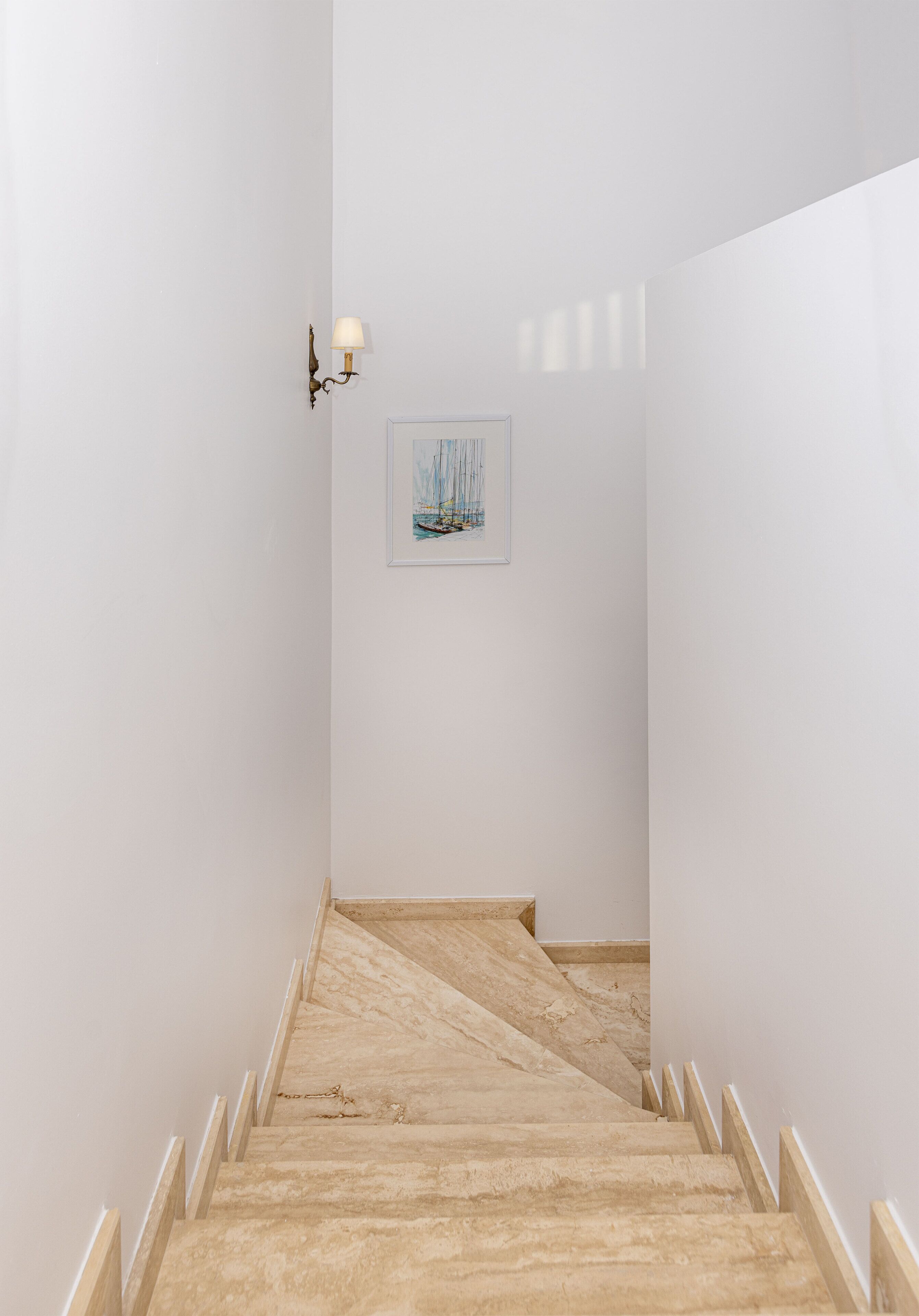 A narrow hallway with a wooden staircase, white walls, and a framed picture on the wall.