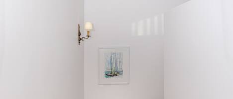 A narrow hallway with a wooden staircase, white walls, and a framed picture on the wall.