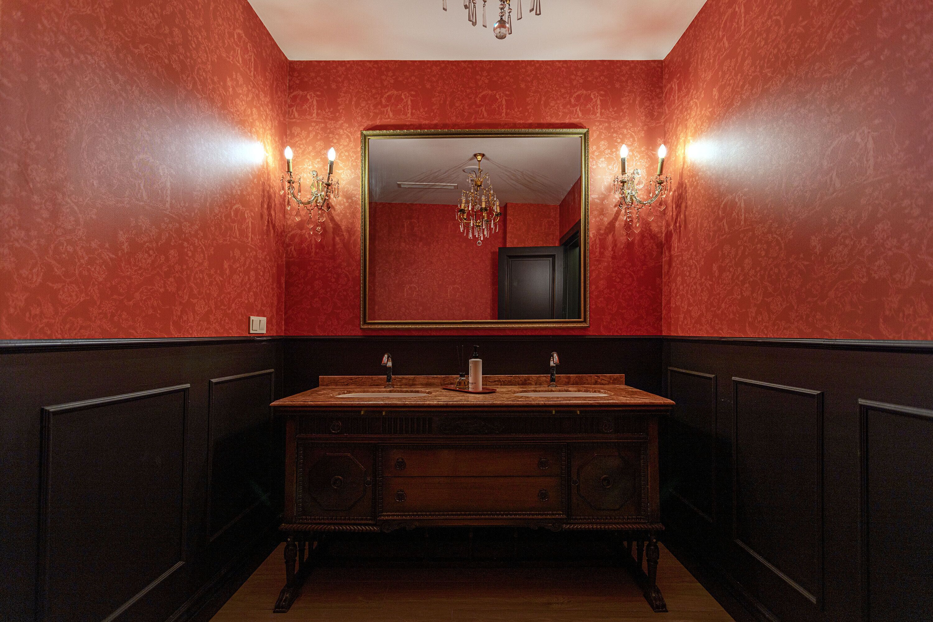 Ein Badezimmer mit einem großen Spiegel, zwei Waschbecken, einer Chandelierleuchtre und Wandleuchten.
