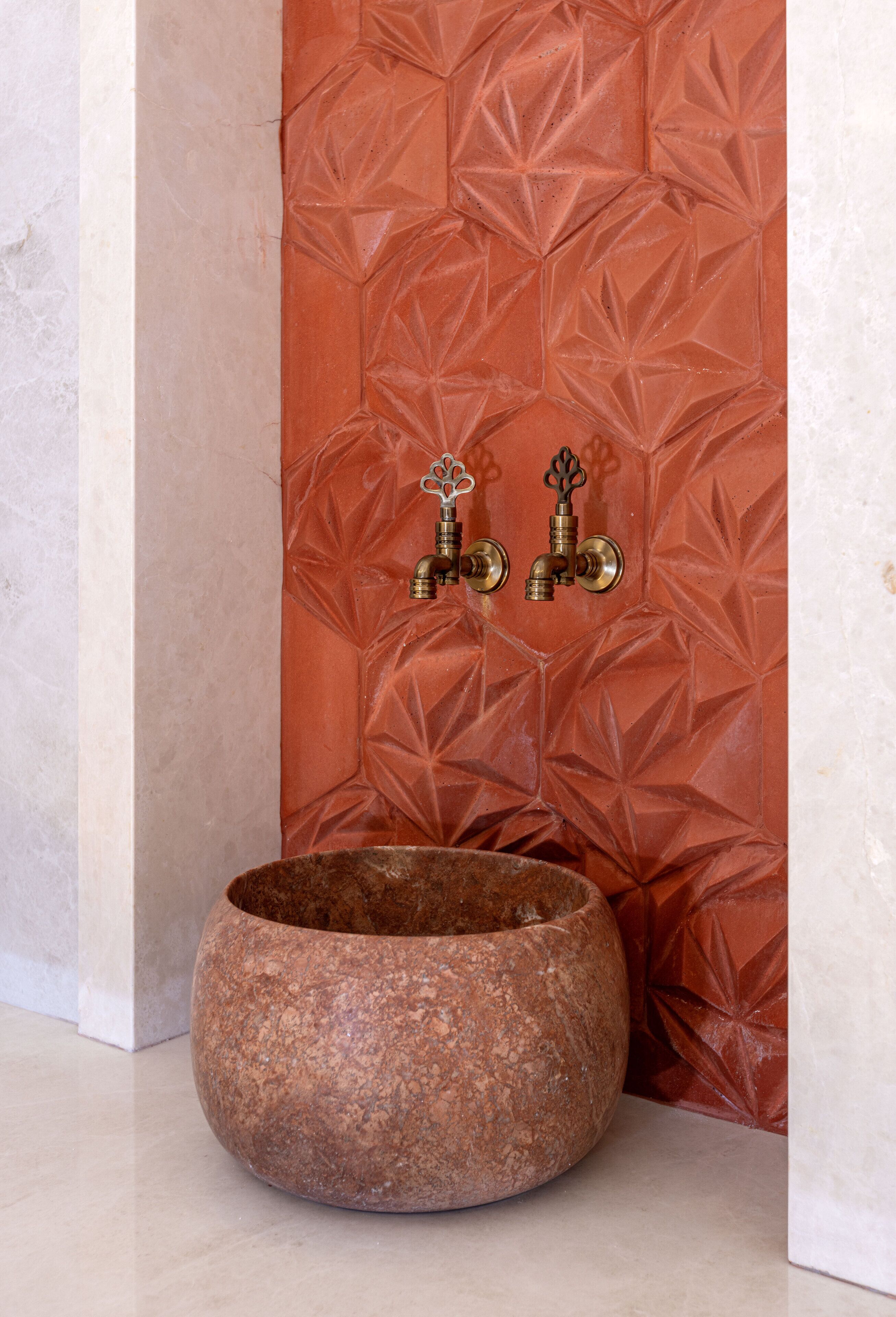 A stone basin in a corner with a textured wall and two brass fixtures.