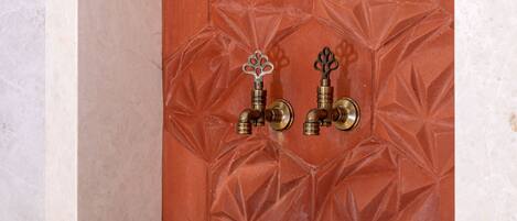 A stone basin in a corner with a textured wall and two brass fixtures.