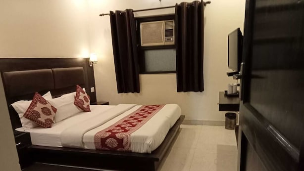 A hotel room with a bed, a chair, a desk with a computer, a TV, and a window with curtains. - Hotel Sunder Palace (Dehradun)