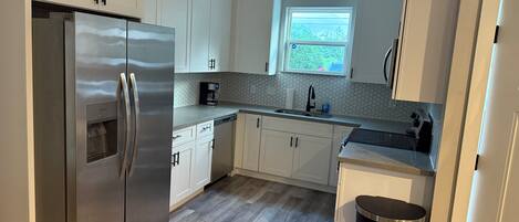 A modern kitchen with white cabinets, a stainless steel refrigerator, a coffee maker, and a window.