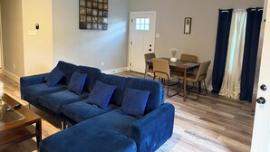 A living room with a blue sectional sofa, a dining table with chairs, a painting on the wall, and a door with curtains. - Charming 3-bedroom 2 bath house in lively Houston (Houston)
