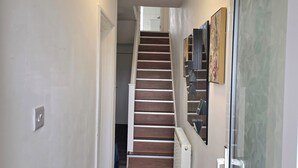 Un pasillo con escalera de madera, un radiador y una puerta que da a otra habitación.