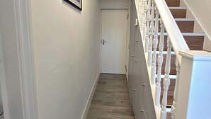 Un pasillo con una escalera de madera, una puerta blanca al final y un cuadro en la pared.