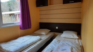Une chambre avec deux lits simples, une fenêtre ornée d’un rideau violet et un téléviseur fixé au mur.