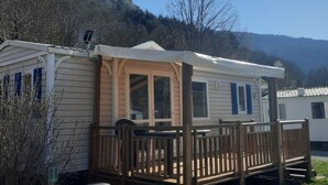 Une maison mobile dotée d’une véranda et d’une fenêtre, entourée d’arbres et de collines.