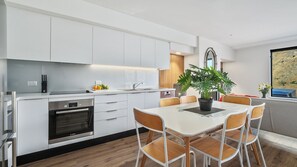 A modern kitchen with white cabinets, a Bosch oven, and a dining area with a white table and wooden chairs. - Shotover River Hideaway - 1 Bed (Queenstown)