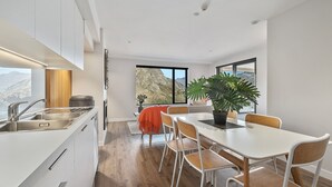 Une cuisine moderne dotée d’une grande fenêtre, un coin repas avec une table et des chaises, et une vue sur les montagnes.