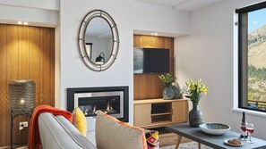 A modern living room with a fireplace, a television, and a view of a mountainous landscape. - Shotover River Hideaway - 1 Bed (Queenstown)