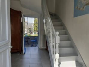 Eine Treppe mit weißen Balustraden, eine Holztür und ein Blick durch ein Fenster auf einen Außenbereich mit Tisch und Stühlen.