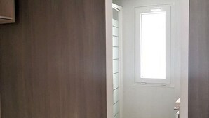 Un couloir avec une porte donnant sur une pièce, un interrupteur et un luminaire fixé au mur.