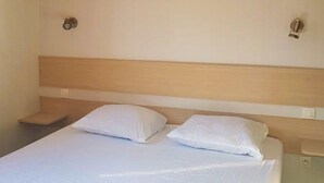 Une chambre d’hôtel avec un lit, deux oreillers, une tête de lit en bois et une petite table de chevet.