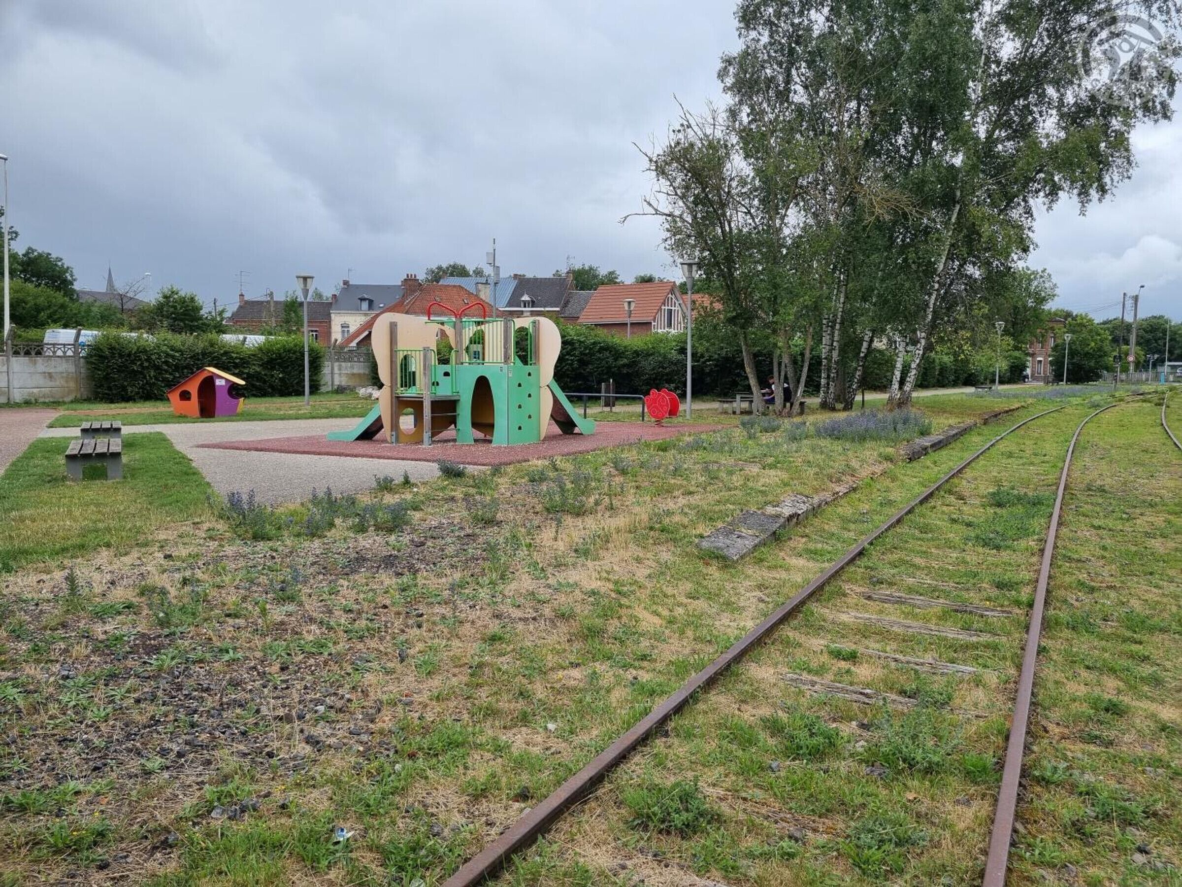 Une aire de jeux avec un toboggan et des structures d’escalade, une petite structure ressemblant à une maison, et une table de pique-nique.