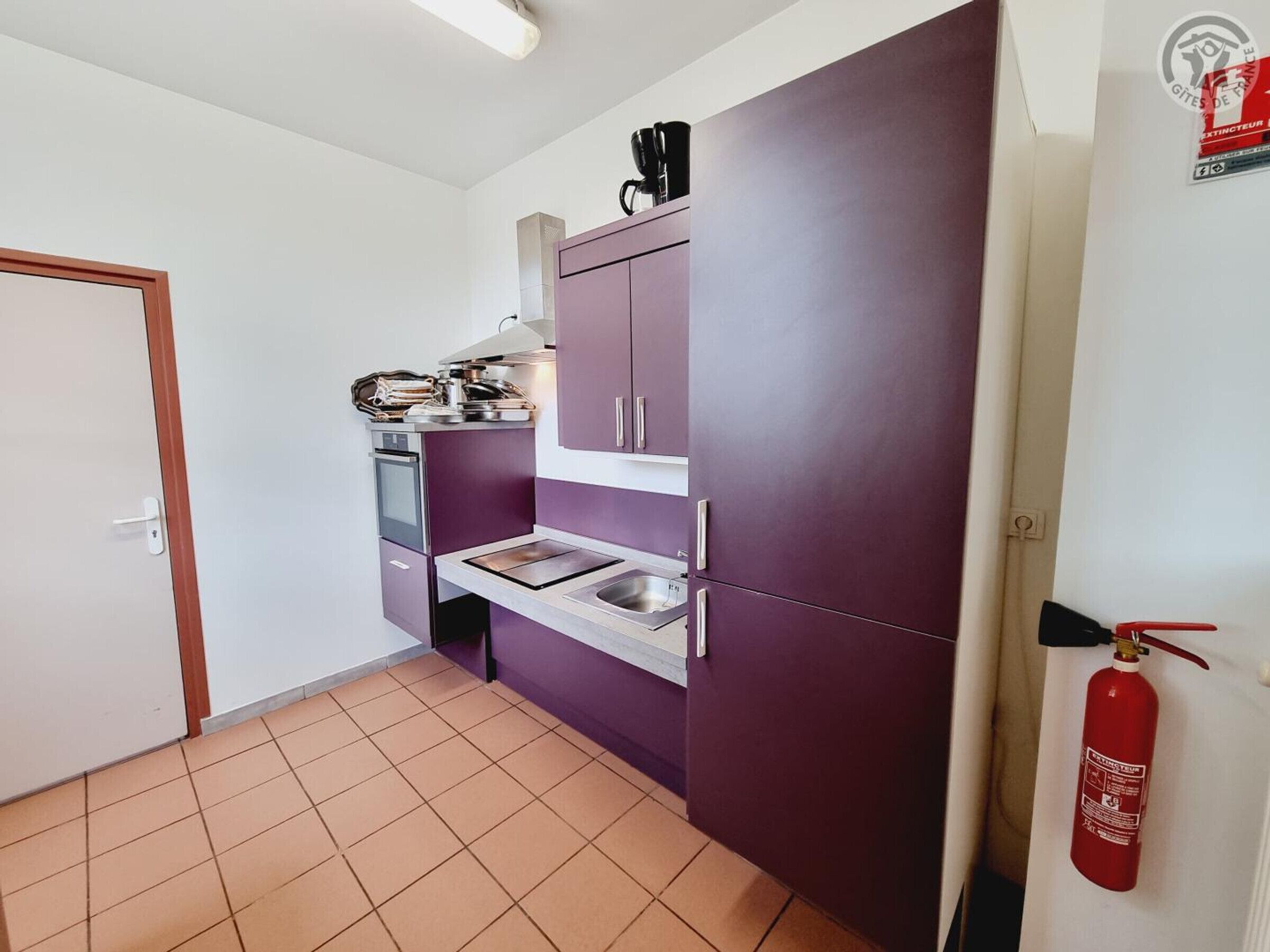 A compact kitchen with a built-in oven, a sink, and a purple cabinet.