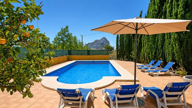 Una piscina con azulejos azules, rodeada de sillones de playa y una sombrilla.