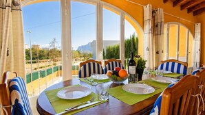 Una mesa de comedor dispuesta con platos, cubiertos, un cuenco de fruta y una botella de vino, con sillas tapizadas en rayas azules y blancas.