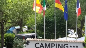 A camping area sign with flags, a tent, and a car.