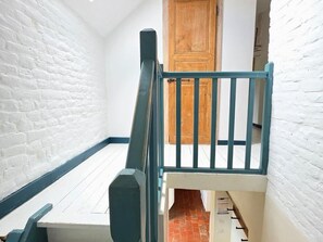 A narrow stairway with a wooden door at the top, white brick walls, and a blue painted handrail.