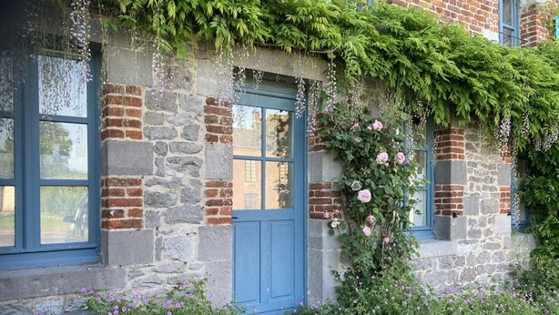 A stone building with a blue door, ivy, and pink flowers.