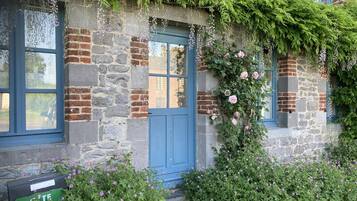 Een stenen gebouw met een blauwe deur, klimop en roze bloemen.