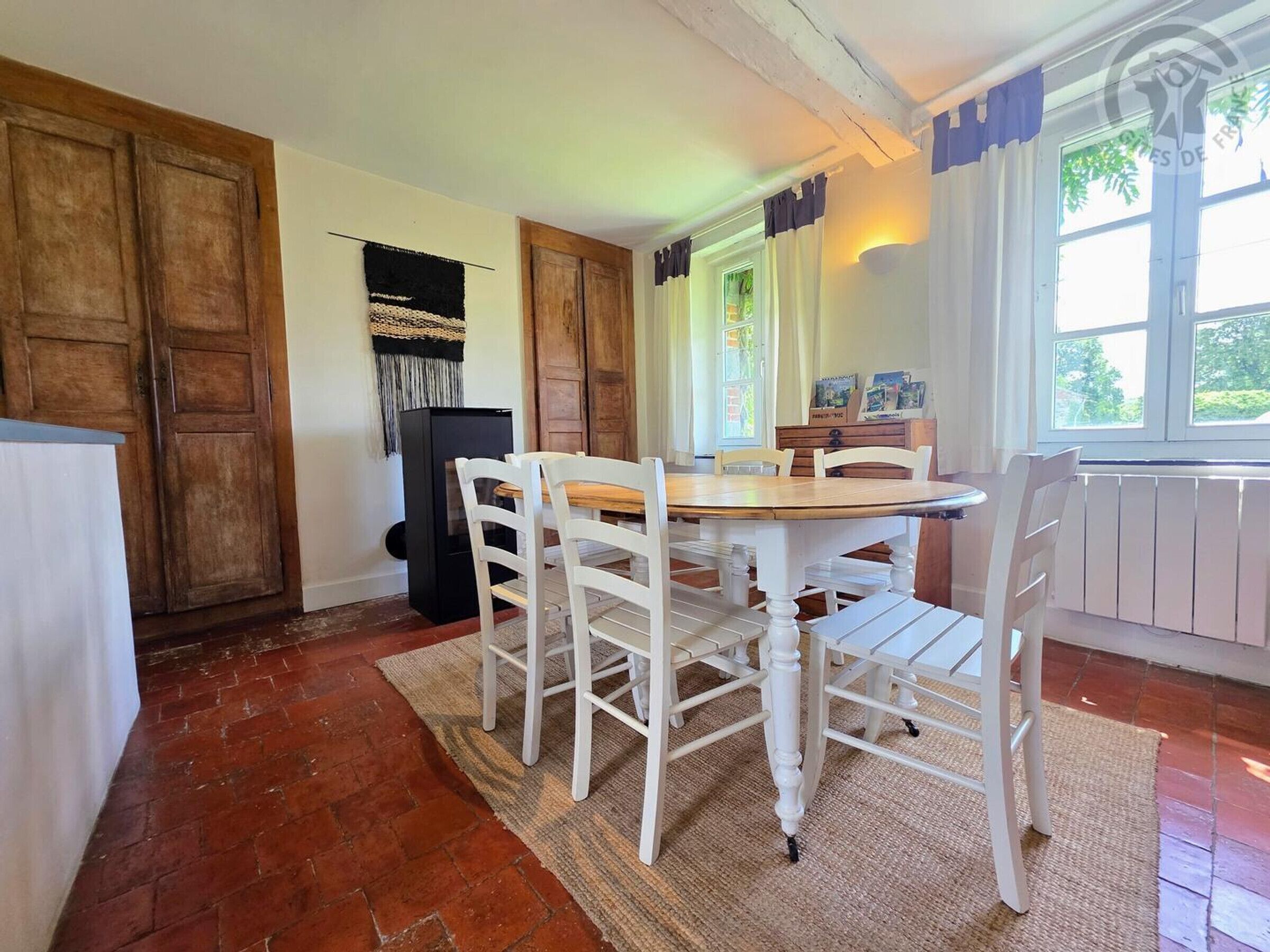 Een eetgedeelte met een houten tafel en witte stoelen, een zwarte koelkast en een raam met gordijnen.