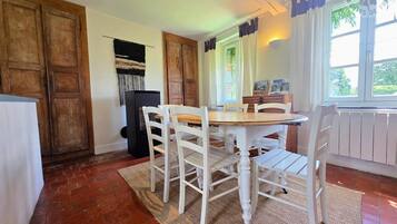 Een eetgedeelte met een houten tafel en witte stoelen, een zwarte koelkast en een raam met gordijnen.