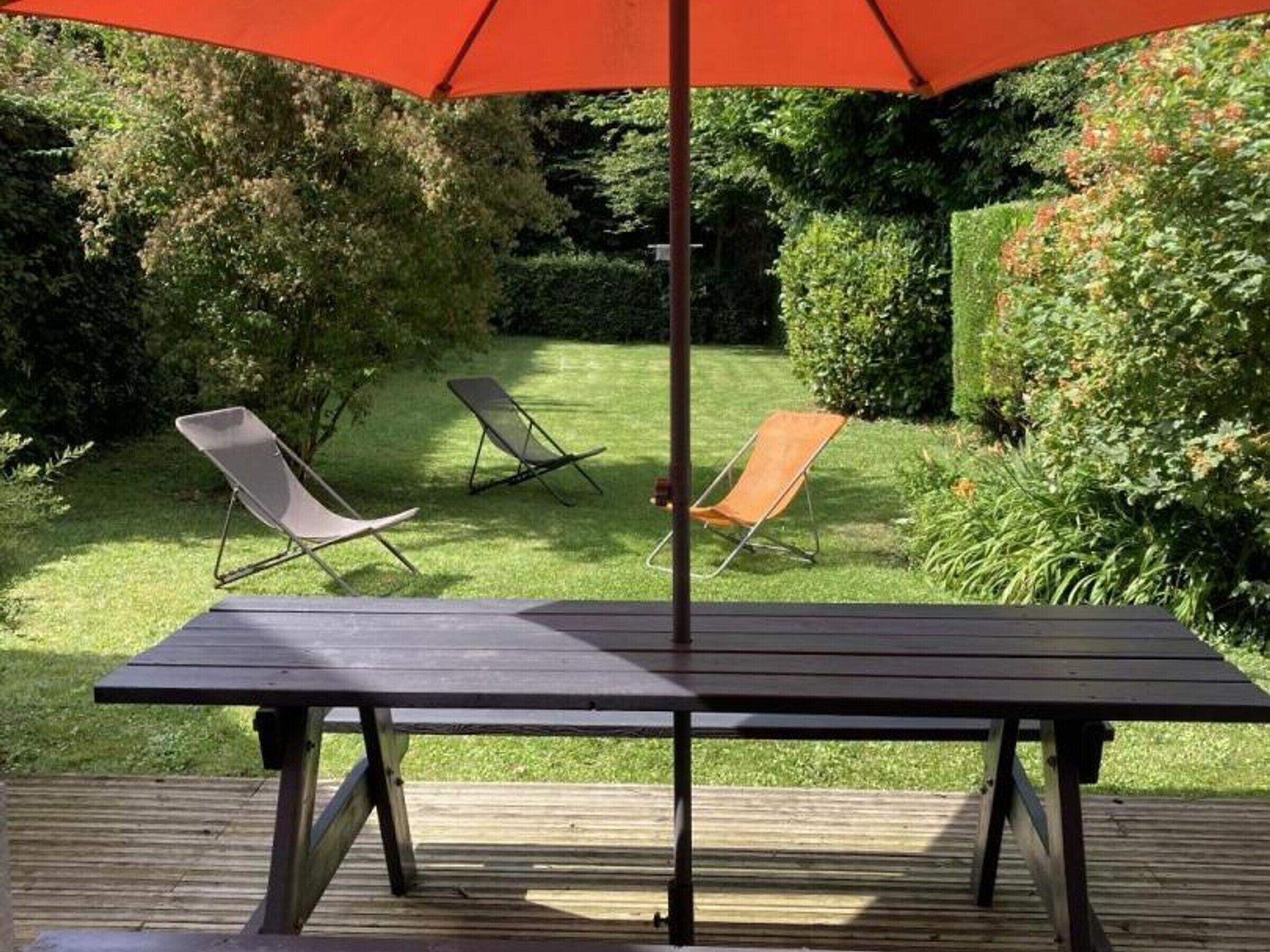 Une terrasse en bois avec une table et deux chaises, protégées par un parasol.