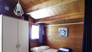 Een kleine kamer met houten lambrisering, een stapelbed, een kledingkast en een enkele lamp.