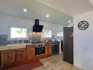 A kitchen with wooden cabinets, a built-in oven, a microwave, a sink, and a refrigerator. - Cozy cottage with garden - 4 guests (LEZIGNEUX)