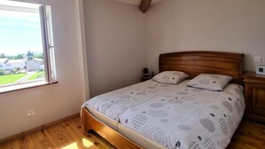 Een slaapkamer met een houten bed, een nachtkastje, een raam met uitzicht en een schuine plafond.