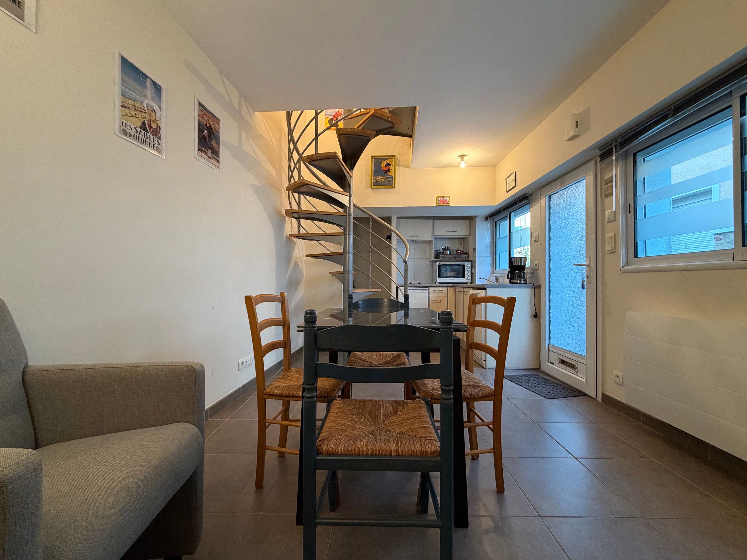 A dining area with a spiral staircase leading to a kitchen, a sofa, and a window with a view.