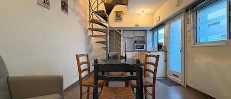 A dining area with a spiral staircase leading to a kitchen, a sofa, and a window with a view.