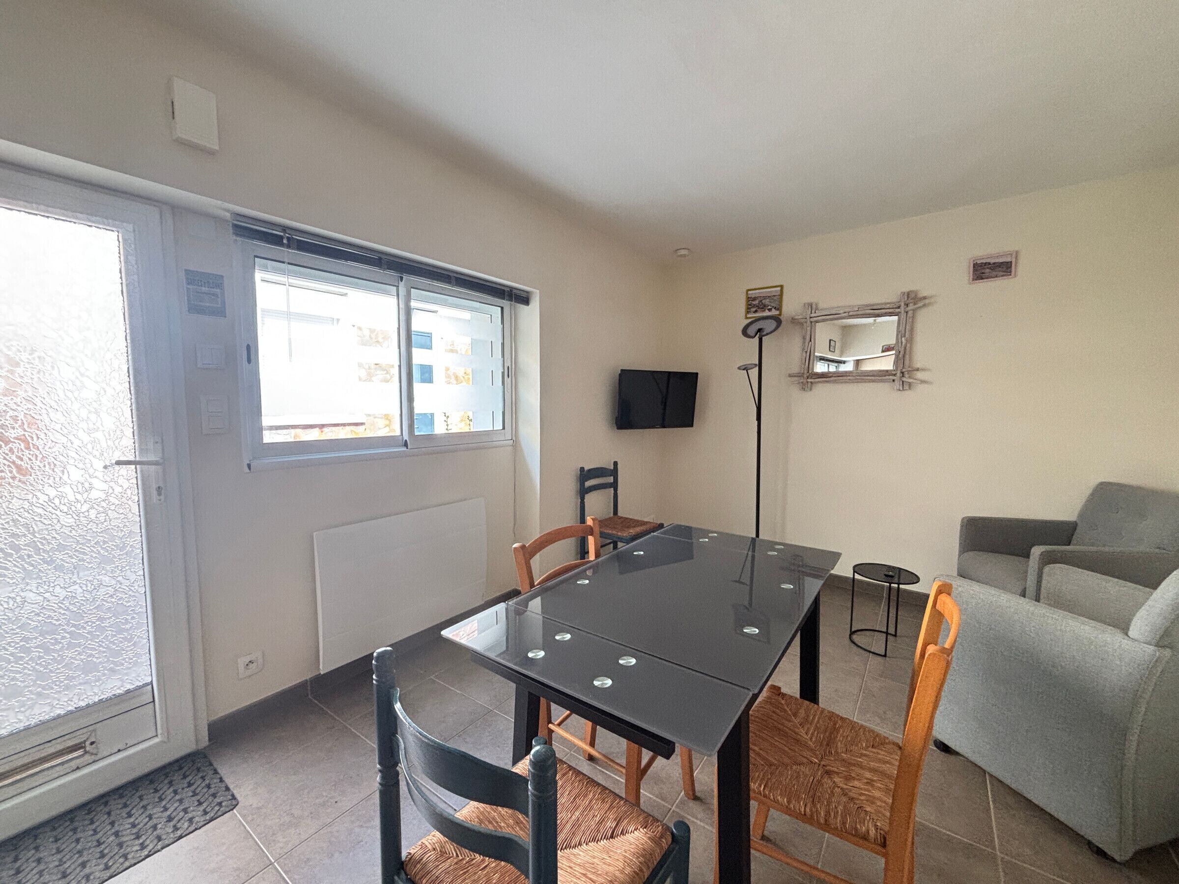 Een kamer met een eettafel, stoelen, een bank, een televisie en een raam.