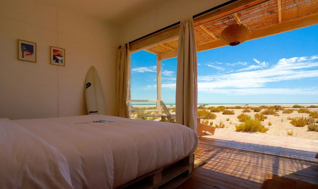 Un dormitorio con cama, una tabla de surf y vistas a la playa.