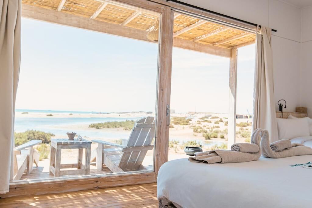 Une chambre avec une grande fenêtre, un lit, une chaise et une petite table.