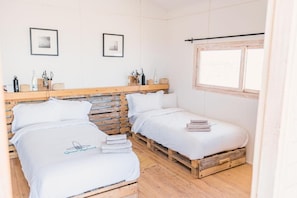 A bedroom with two beds, wooden headboard, white bedding, a window, and framed pictures on the wall. - OCEAN VAGABOND LASSARGA (Dakhla)