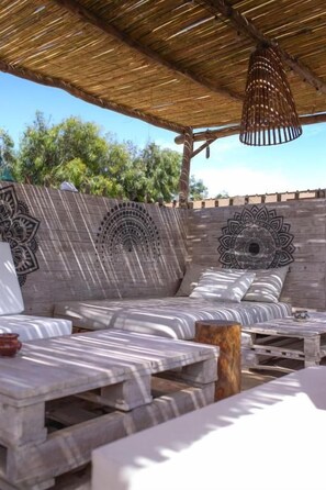 An outdoor seating area with patterned cushions, wooden tables, and a thatched roof.