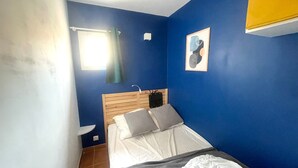 Una camera da letto con una testiera in legno, un letto con biancheria bianca, un piccolo comodino, una finestra con tenda e un punto luce a parete.