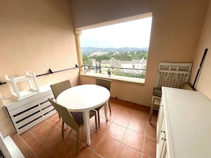 Ein Balkon mit Tisch und Stühlen, Blick auf eine Stadtlandschaft und ein Fenster mit Metallgitter.