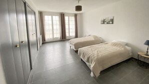 Ein Schlafzimmer mit zwei Betten, einem Kleiderschrank, einem Fenster mit Vorhängen und einem kleinen Tisch mit Lampe.
